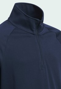 Pull-over demi-glissière bleu marine avec un col montant. Tissu lisse et extensible avec des manches raglan pour un grand confort de mouvement. Détail de fermeture éclair au niveau du col.