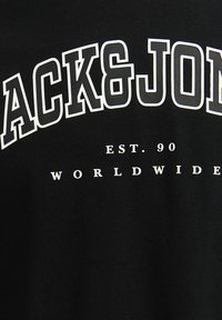 Fekete pamut póló, nagy, fehér, nagybetűs felirattal: "BACK&JON" és kisebb "EST. 90 WORLDWIDE" felirattal középen alatta. Táltos mintázatú anyag.