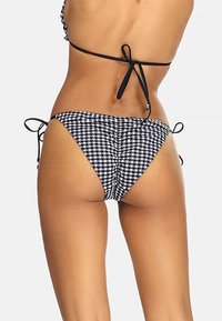 Czarny i biały bikini w kratkę z regulowanymi sznureczkami po bokach, o niskim stanie i gładkiej fakturze.