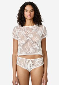 Completo di lingerie bianca in pizzo con motivi floreali; crop top a maniche corte e pantaloni corti abbinati, decorati con bordi scallop e vita con coulisse.