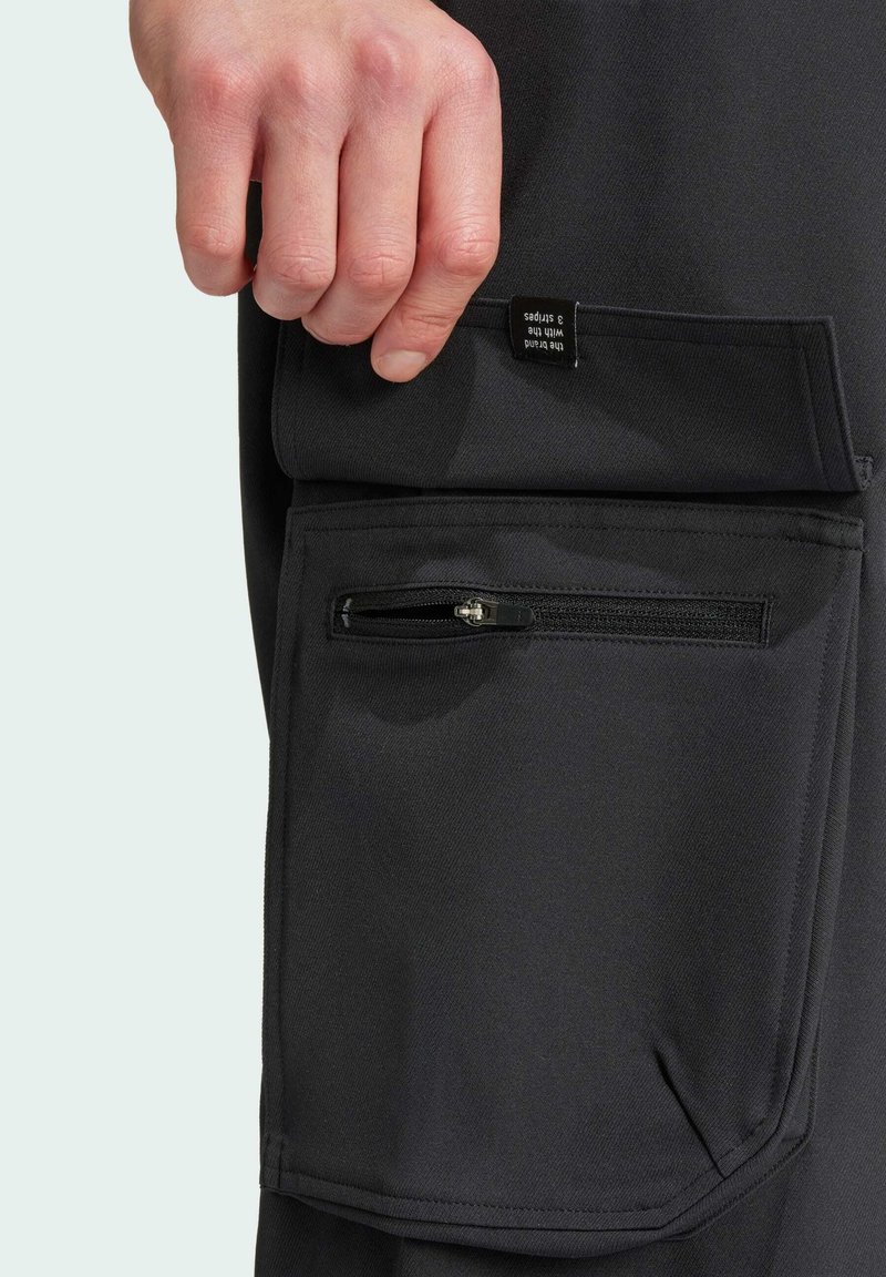 Schwarze Cargo-Hose mit einer großen Seitentasche und einer kleineren Reißverschlusstasche. Der Stoff hat eine strukturierte Oberfläche mit sichtbaren Nähdetails.