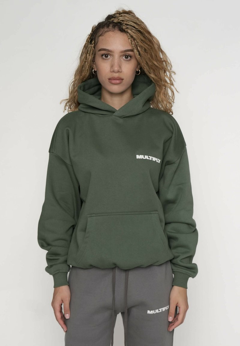Groene hoodie met een voorzak en geribde manchetten, met het woord "MULTIPLY" in het wit op de linkerborst. Grijze joggingbroek maakt de outfit compleet.