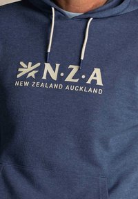 Marineblauwe hoodie van zachte stof met een kangoeroezak, met daarop witte tekst "N.Z.A. NIEUW-ZEELAND AUCKLAND" en een sterlogo.