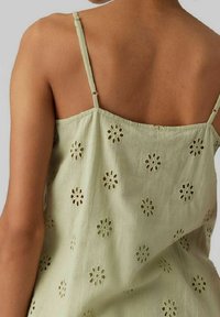 Ljusgrön ärmlös topp med blommiga utskärmningsmönster, tillverkad av ett mjukt, strukturerat tyg; har tunna axelband och en lös passform.