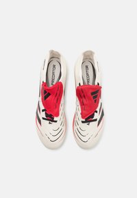 White athletic shoes with red accents, featuring a textured material, sleek design, and distinct black stripes on the sides.