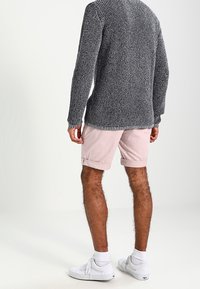 Grauer Strickpullover, hellrosa Shorts, weiße Sneakers. Der Pullover hat ein strukturiertes Muster; die Shorts sind über dem Knie gekrempelt.