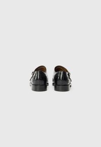 Pantofi din piele neagră cu un finisaj lustruit, cu vârful rotund și toc mic. Detalii decorative de brogue pe laturi și pe spate.