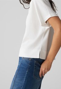 Hvid tekstureret bluse med korte ærmer, med sideslids, parret med blå denimjeans. Silhuetten er afslappet og casual.