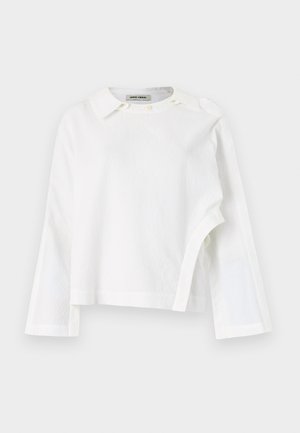 Camicia bianca a maniche lunghe realizzata in un tessuto testurizzato, con colletto classico e chiusura a bottoni al collo, dotata di un orlo asimmetrico.