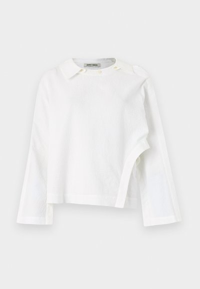 Hvit langermet skjorte med teksturert stoff, klassisk krage og knappelukking i nakken, samt asymmetrisk kant.