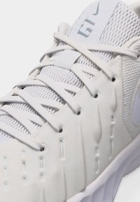 Κοντινό πλάνο λευκού αθλητικού παπουτσιού με επάνω μέρος από δίχτυ, υφή στις πλευρικές επιφάνειες και λευκά κορδόνια δεμένα πάνω στη διαπνέουσα γλώσσα.