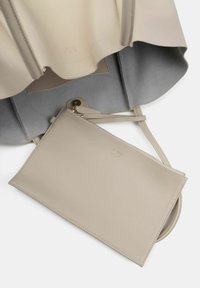 Beige nahkakäsipussi, jossa on viistetty yläreuna, harmaalla mokkanahka sisustalla ja siihen sopiva irrotettava vetoketjullinen pussi.