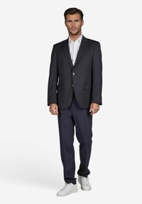 Marineblazer mit goldenen Knöpfen, weißem Hemd und dunklen Hosen. Abgerundet mit weißen Sneakers für einen modernen, lässigen Look.