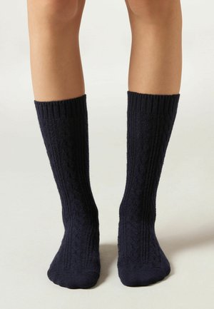 Calze a maglia blu navy alte fino al ginocchio con una texture a coste e un sottile motivo a trecce. Tessuto liscio, punta arrotondata e bordo elastico.