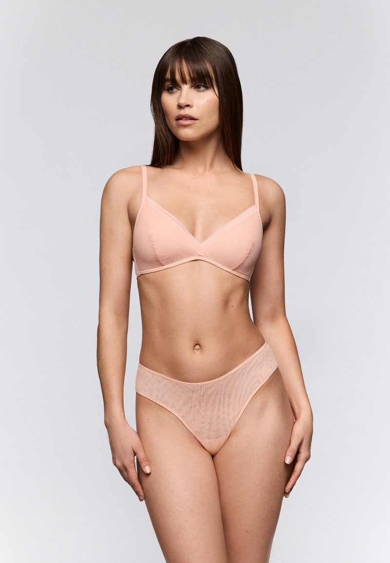 Conjunto de bralette y tanga en color durazno suave, hecho de un tejido transparente con textura acanalada, que presenta tirantes finos y un diseño minimalista.