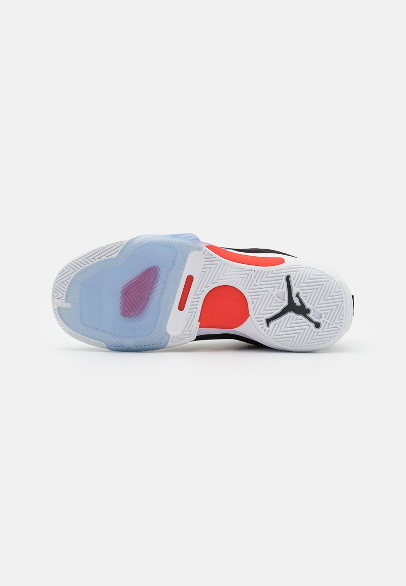 Semelle de chaussure de basketball avec une section bleue translucide, des accents rouges, une base blanche texturée avec un logo noir et un motif en chevrons.
