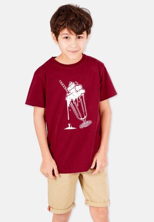 Burgunder Baumwoll-T-Shirt mit einem weißen Eisbecher-Grafik und einem Strohhalm, kombiniert mit hellbeigen Shorts. Glatte Textur.