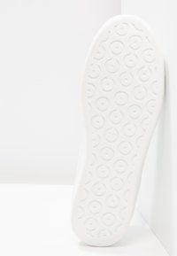 Bílá podrážka boty s texturovaným, kruhovým vzorem. Číslo "37" je viditelné. Okraj je hladký a zaoblený, což kontrastuje s texturovaným povrchem.