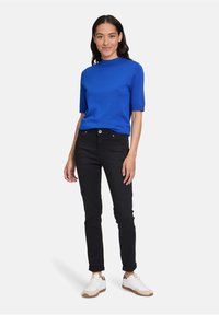 Modrý krátký rukáv top s vysokým výstřihem, spárovaný s černými slim fit džíny a bílými teniskami s hnědými akcenty.
