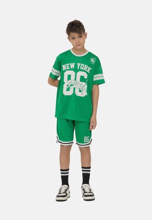 L'outfit sportivo in rete verde presenta una stampa 'NEW YORK 86', una grafica di tigre bianca e accenti contrastanti in bianco e nero sulle maniche e sui pantaloni. 