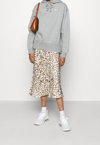 Felpa grigia con cappuccio e cordino, gonna midi con stampa leopardata bianca e marrone, sneakers bianche e piccola borsa a tracolla marrone.