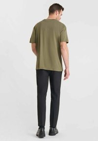 Camiseta de manga corta verde oliva con un corte relajado, combinada con pantalones oscuros texturizados y zapatos negros. Diseño simple y minimalista.