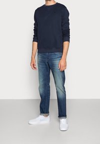 Marineblaues Sweatshirt mit Rundhalsausschnitt und gerippten Bündchen, kombiniert mit ausgewaschenen blauen Jeans und weißen Turnschuhen. Lässiges Outfit mit entspannter Passform.