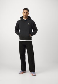 Hanorac negru cu glugă, dotat cu buzunar frontal și logo alb, asortat cu pantaloni negri și adidași gri cu accente portocalii.