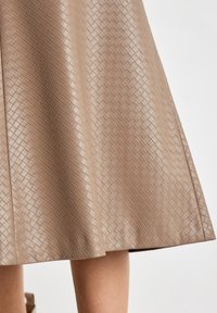 Beige faux lædernederdel med et struktureret diamantmønster. A-formet design og knælængde, med en glat, skinnende finish.