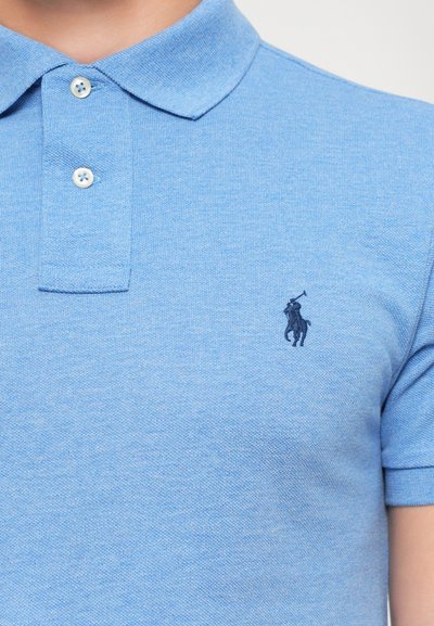 Lichtblauw polo-shirt in een gestructureerde brei, met een drieknoopsluiting en een klein donkerblauw geborduurd logo op de linkerkant van de borst.