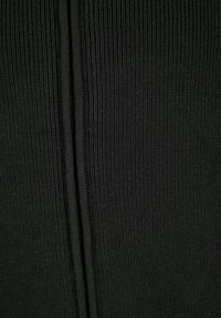 Schwarzer gerippter Stoff mit einer strukturierten Oberfläche, der eine zentrale Naht aufweist, die dem Design Dimension verleiht. Das Material wirkt dehnbar und langlebig.