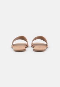 Sandales à glissière en cuir tan avec deux sangles incurvées, semelles plates et un minimalisme dans les coutures. Texture lisse, design simple, sans marque visible.