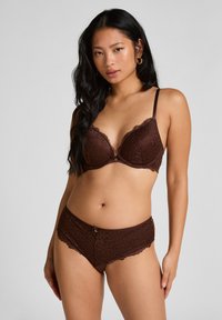 Bra aus brauner Spitze mit gewellten Kanten und einem kleinen dekorativen Knopfdetails, kombiniert mit passenden braunen Spitzenshorts im ähnlichen Design.