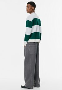 Grün-weiß gestreifter Pullover mit Kragen, kombiniert mit lockeren grauen Jeans. Der Pullover hat gerippte Bündchen und einen Saum.