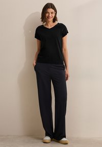Haut noir à manches courtes en V associé à un pantalon large bleu marine, doté de poches latérales et d'une coupe décontractée. Design uni sans motifs visibles.