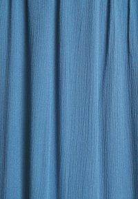 Skrynklig tyg i en medelblå nyans, med mjuk textur och vertikala linjer, draperad i vecken, vilket betonar en lätt utseende.