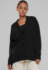 Svart oversized cardigan laget av teksturert stoff, med dyp V-hals, frontlukking med knapper og ribbestrikket kant og mansjetter.