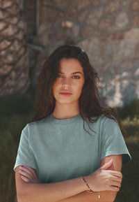 Ljus teal bomull t-shirt med rundad halsringning och korta ärmar, som har en mjuk struktur mot en naturlig utomhusbakgrund.