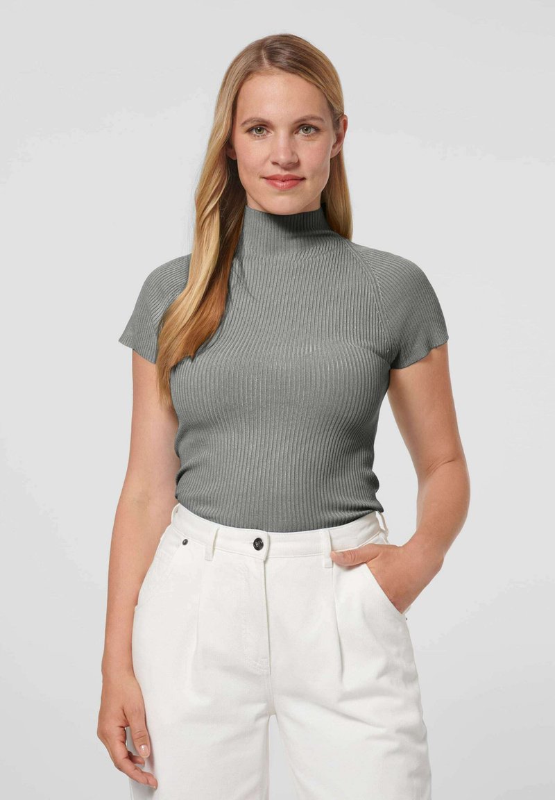 Grijze geribbelde turtleneck met korte mouwen, strak ontwerp. Gecombineerd met hoge witte broeken, met een knoop aan de voorkant en zakken.