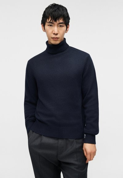 Μπλε ζιβάγκο πουλόβερ από μαλακό πλεκτό ύφασμα με ριγέ γιακά, τελείωμα και μανσέτες, σε συνδυασμό με γκρι παντελόνι με λεπτές ρίγες.