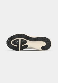 Semelle de chaussure de sport noire et blanche avec un motif antidérapant texturé et un design segmenté pour l'adhérence, vue par dessous sur un fond uni.