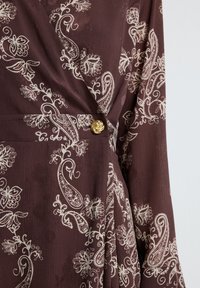Braunes Kleid mit weißen Blumen- und Paisleymustern, strukturiertem Stoff und einem goldenen dekorativen Knopf an der Taille.