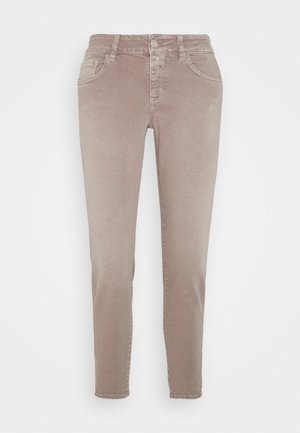 Beżowe spodnie o wąskim kroju z przodem na guzik, zamkiem błyskawicznym, szlufkami na pasek i dwoma przednimi kieszeniami na białym jednolitym tle.