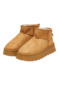 Tanfarbige Wildleder-Stiefeletten mit strukturierter Oberfläche, die eine dicke Plateausohle und ein weiches, flauschiges Innenfutter aufweisen. Abgerundete Zehenpartie und Zuglasche an der Rückseite.