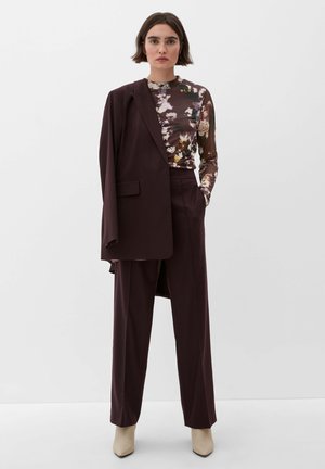 Bordeauxpak met losse broek en gestructureerde blazer, gelaagd over een bloemen-t-shirt met lange mouwen in verschillende gedempte kleuren.