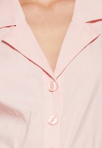 Light pink button-up shirt featuring a pointed collar, four matching buttons, and a smooth, textured fabric.