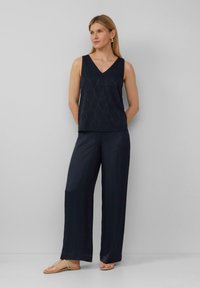 Marineblaue ärmellose Bluse mit einem strukturierten Blattmuster, kombiniert mit weit geschnittenen marineblauen Hosen und beigefarbenen Sandalen. Minimalistisches Design.