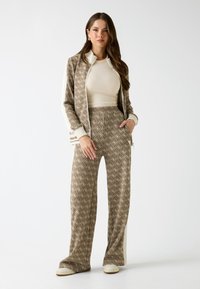 Brązowy dres w wzory z kremowymi akcentami; zapinana kurtka, dopasowany top i szerokie spodnie. Miękka tekstura i dekoracyjne detale wzornicze.