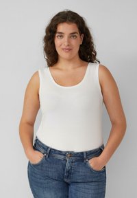 Witte, mouwloze top met een ronde halslijn, gemaakt van zachte stof. Gecombineerd met donkerblauwe denim jeans met een knoop en zakken.