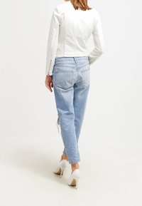 Vit faux läder kort jacka med perforerade paneler, i kombination med ljusblå slitna jeans och vita högklackade skor.